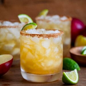 Glasses on Apple Cider Margarita on a wooden table and wooden plate with fresh apple and limes.