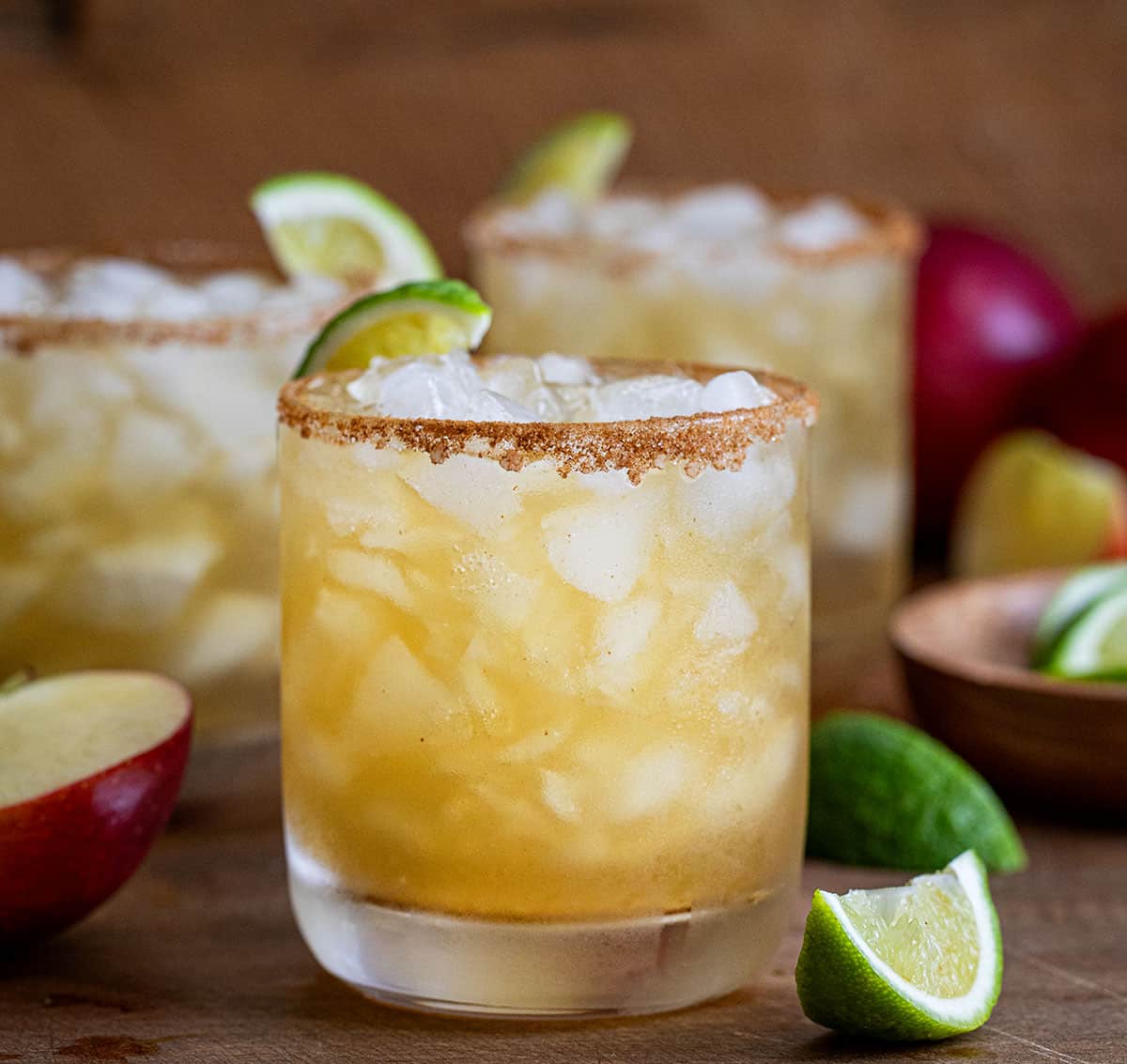 Glasses on Apple Cider Margarita on a wooden table and wooden plate with fresh apple and limes.