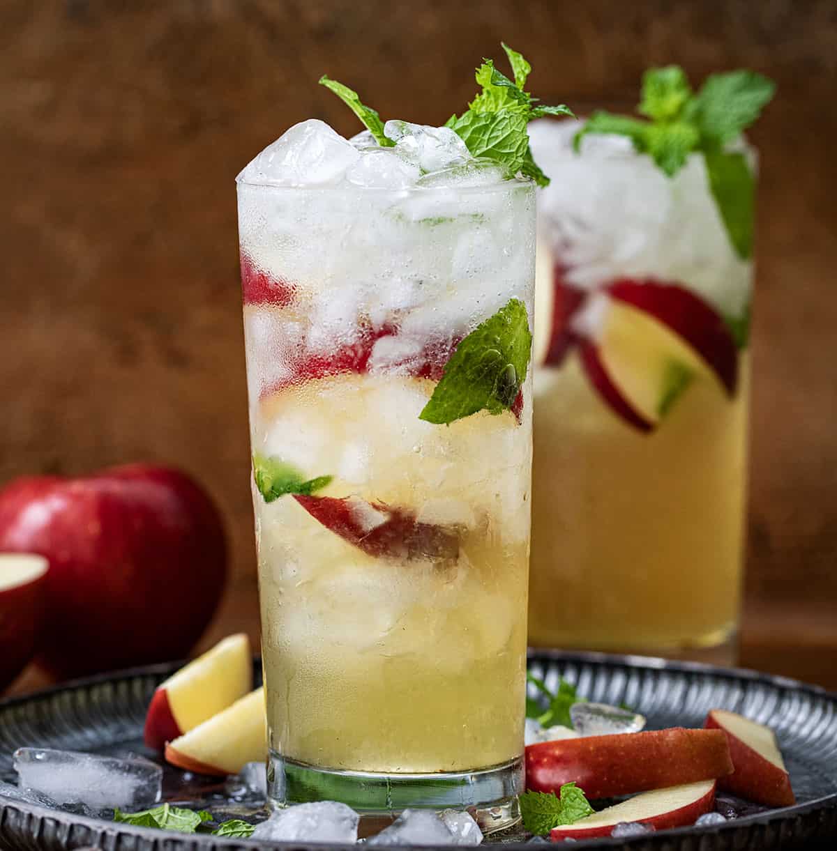 Glasses of Apple Cider Mojito on a tray with crushed ice and mint and apple slices.