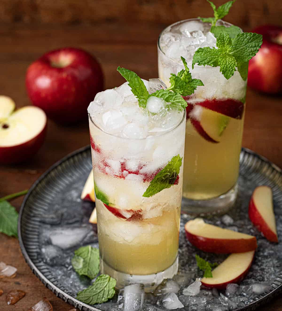 Glasses of Apple Cider Mojito on a tray with crushed ice and mint and apple slices.