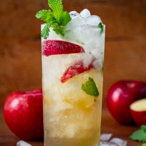 Glass of Apple Cider Mojito on a wooden table with apples and mint.