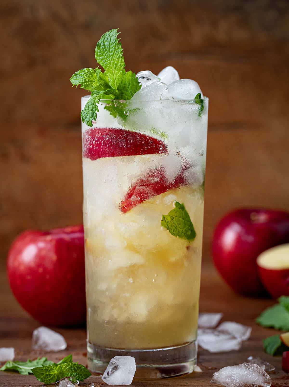 Glass of Apple Cider Mojito on a wooden table with apples and mint.