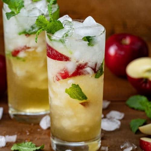 Glasses of Apple Cider Mojito on a wooden table with apples and mint.