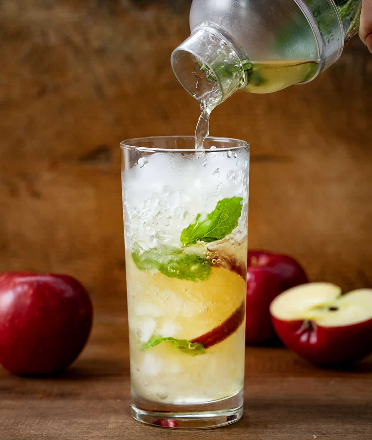 Pouring Apple Cider Mojito into a glass of ice and apple slices.