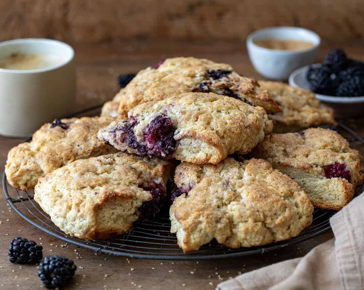 Rack with Blackberry White Chocolate Scones on it on a wooden table with fresh blackberries around.