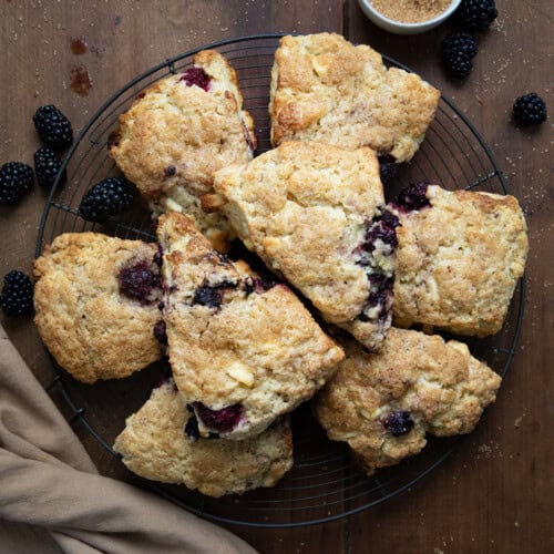 Rack with Blackberry White Chocolate Scones on it on a wooden table with fresh blackberries around.