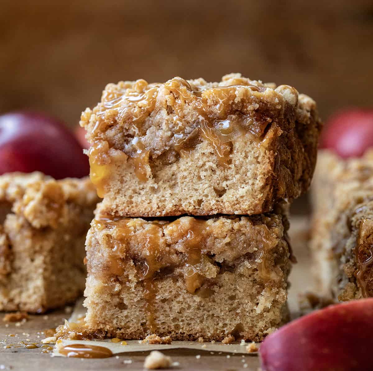 Stack of Caramel Apple Crumb Cake on a wooden table with fresh apples and caramel.