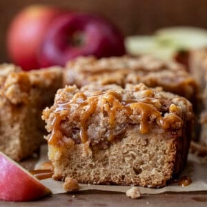 Caramel Apple Crumb Cake on a wooden table showing caramel drizzle and fresh apples.