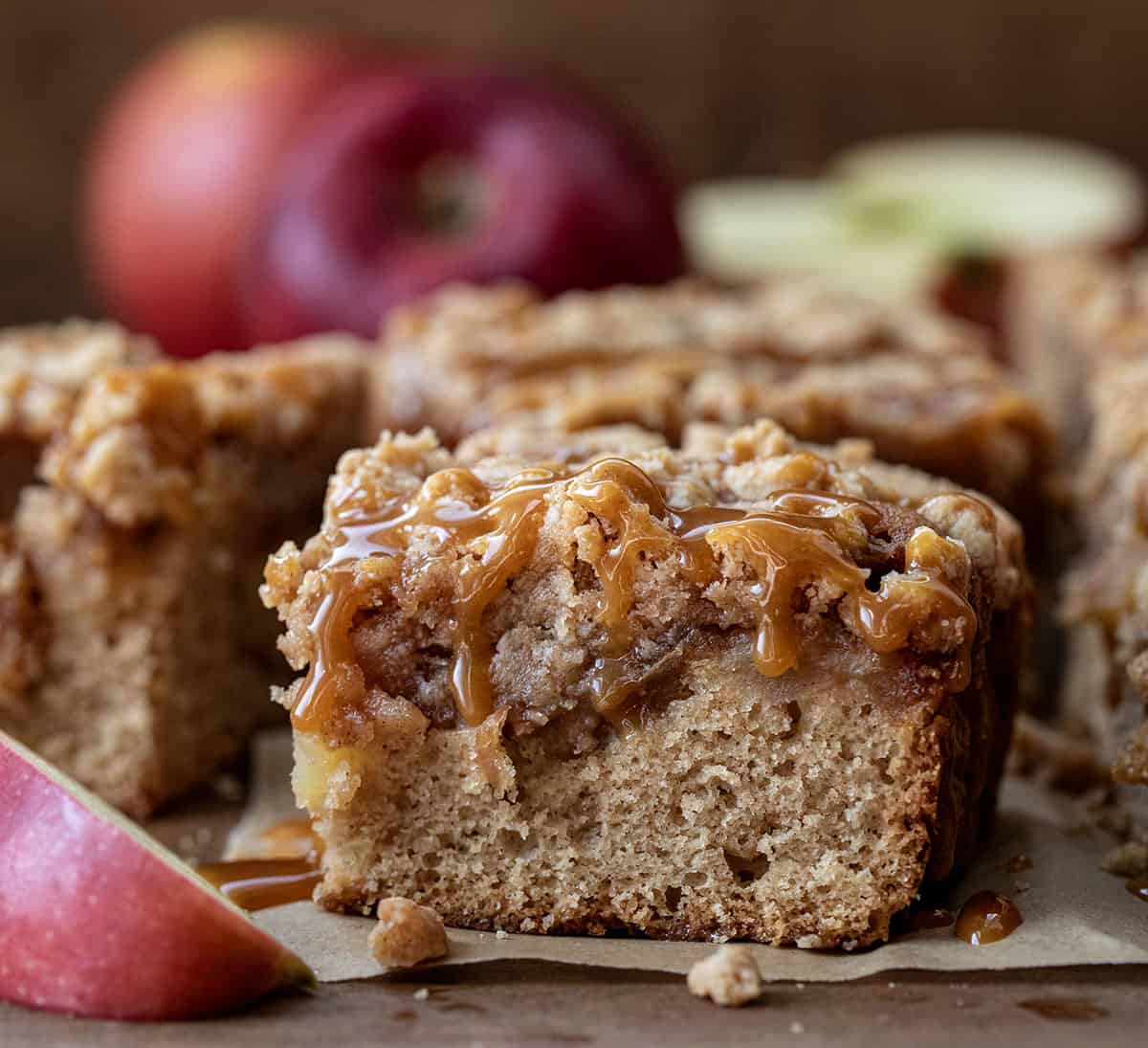 Caramel Apple Crumb Cake on a wooden table showing caramel drizzle and fresh apples.