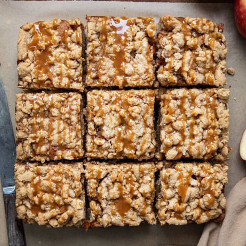 Caramel Apple Crumb Cake cut into slices on parchment paper on a wooden table from overhead.