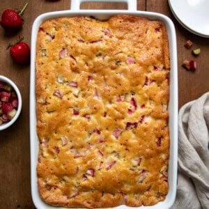 Whole Fresh Strawberry Rhubarb Cake in a white cake pan on a wooden table from overhead.