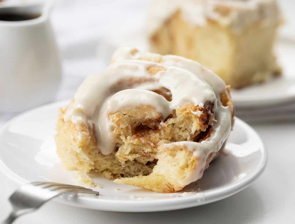 Maple Cinnamon Roll on a white plate with a bite taken out with a fork resting on the edge.