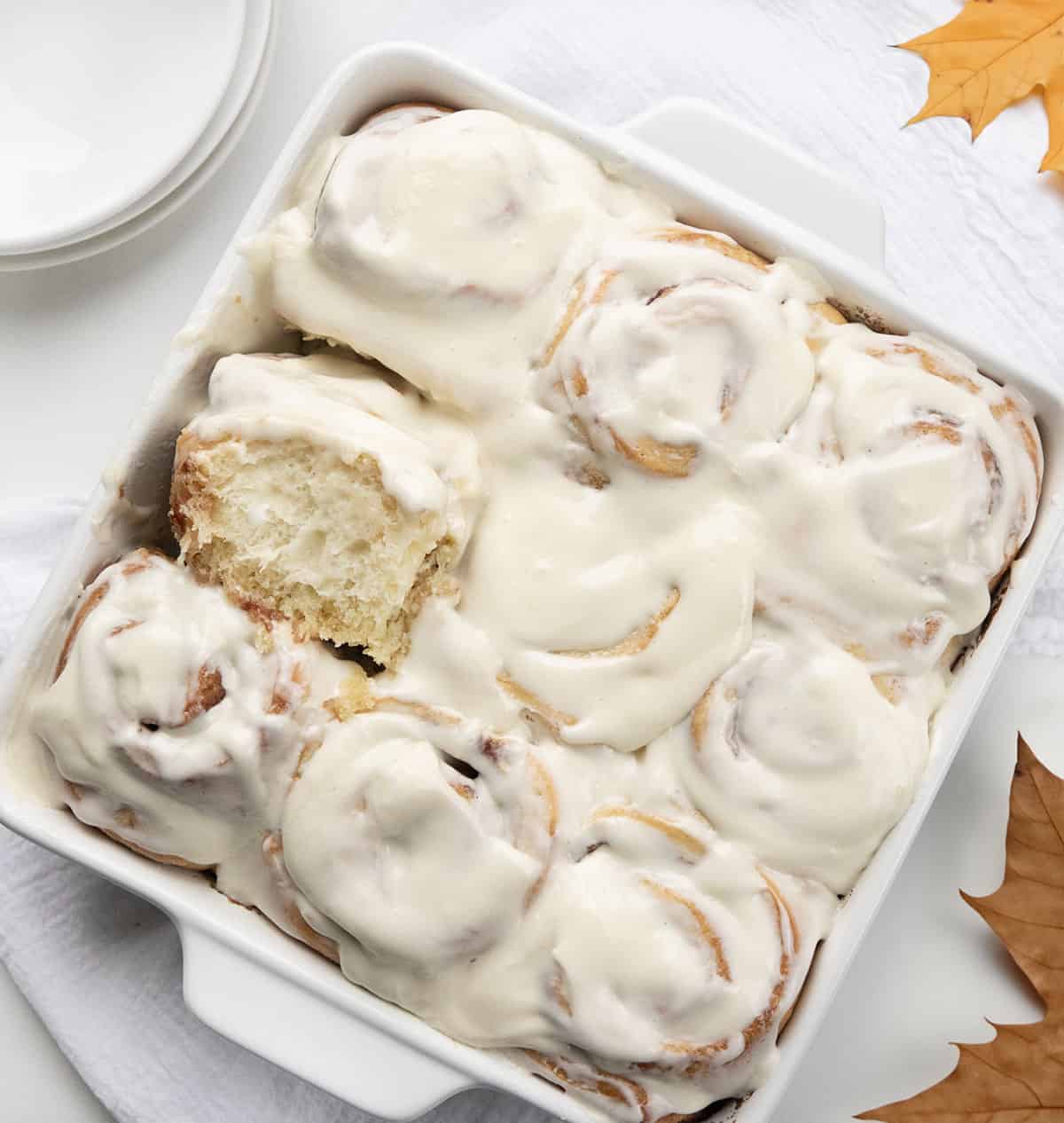 Pan of Maple Cinnamon Rolls on a white table with maple leaves from overhead.