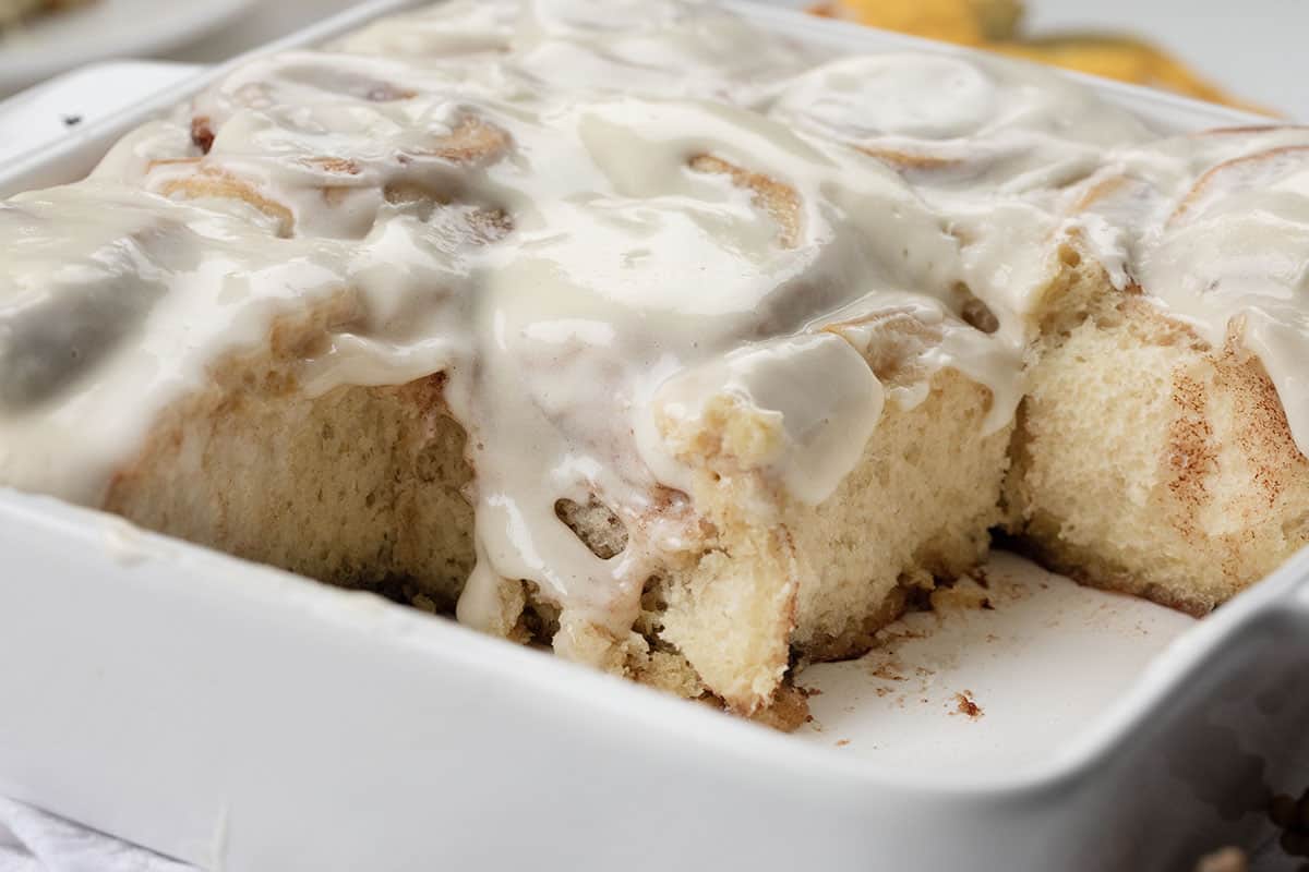 Pan of Maple Cinnamon Rolls with some missing showing the texture and maple whipping icing.