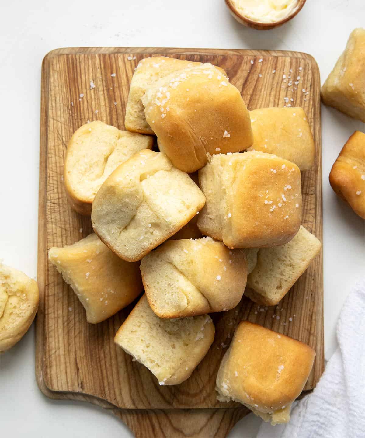 Parker House Rolls on a wooden cutting board on a white table from overhead.