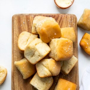 Parker House Rolls on a wooden cutting board on a white table from overhead.