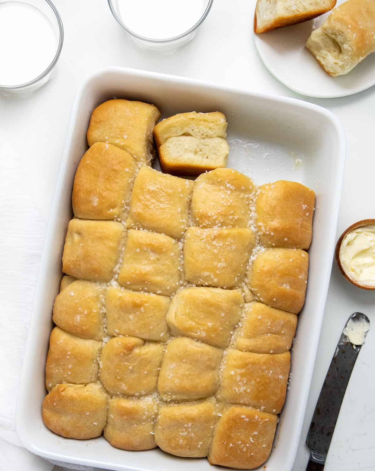 Parker House Rolls in a dish with one roll removed on a white table. 