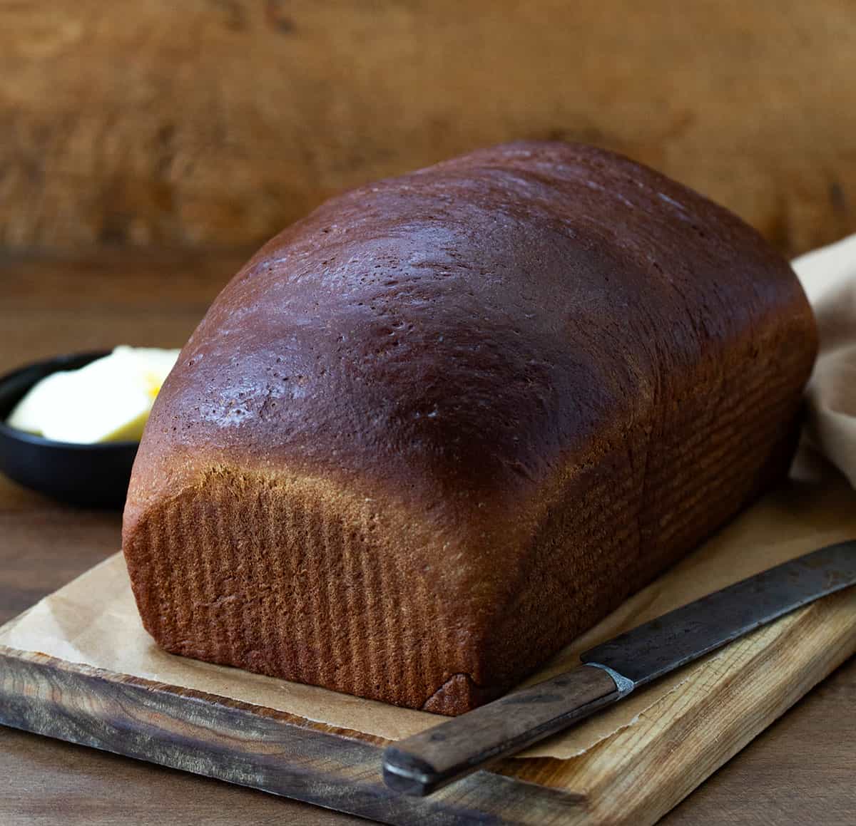 Whole Pumpernickel Bread loaf on a cutting board on a wooden table. 