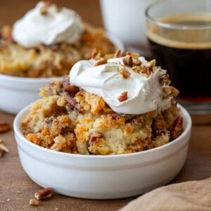 Bowls of Sweet Potato Dump Cake on a wooden table topped with whipped cream and next to a cup of coffee.