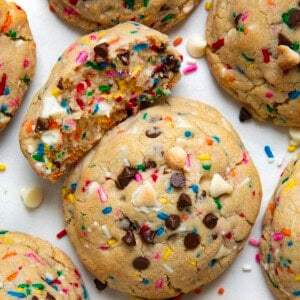 Thick and Chewy Sprinkles Cookies on a white table with one cookie halved showing inside texture.