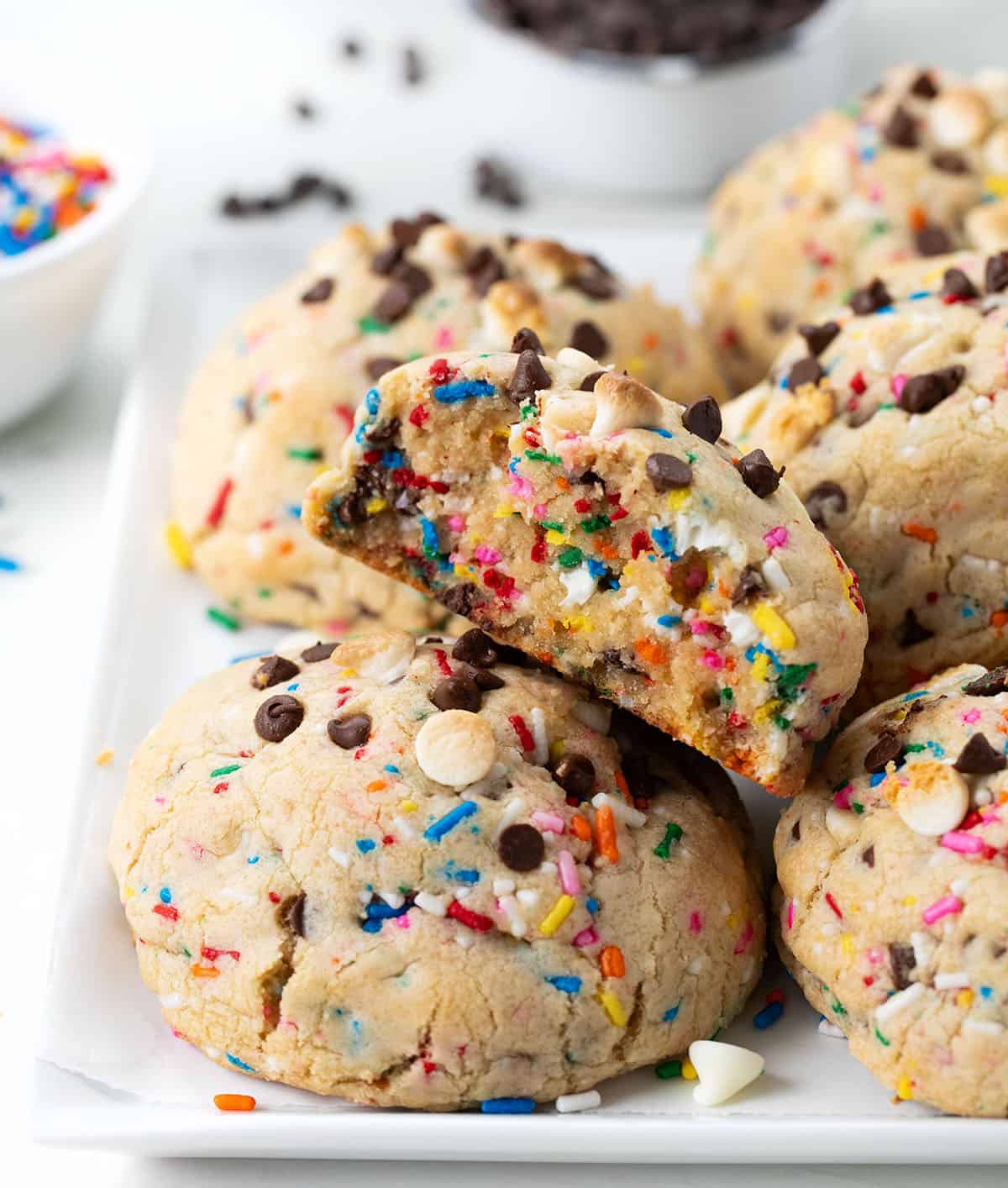 Plate of Thick and Chewy Sprinkles Cookies with one cookie halved showing inside texture.