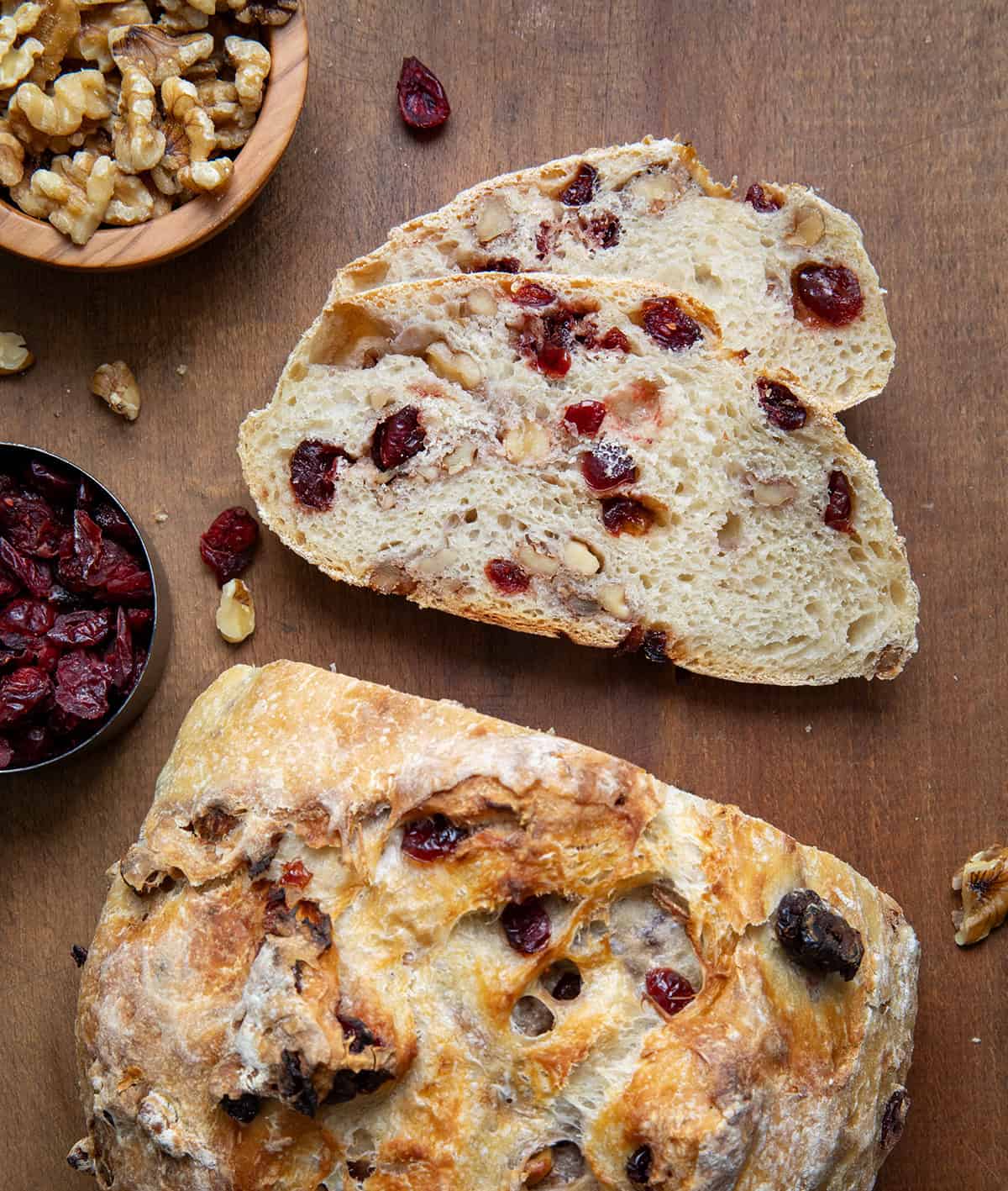 Cranberry Walnut Bread on a wooden table with pieces sliced off and laying flat showing the tender crumb.