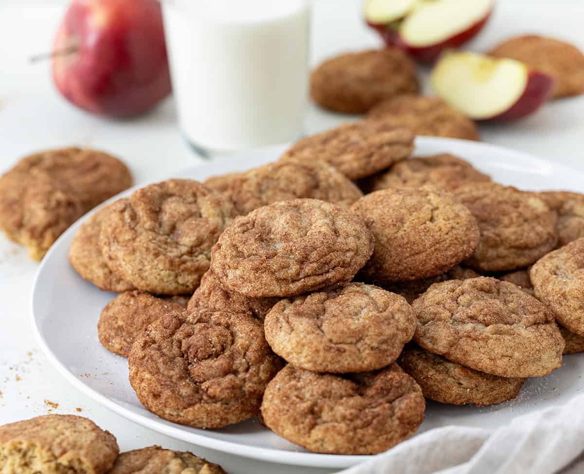 Plate of Apple Butter Snickerdoodles with glass of milk and fresh apples on a white table.