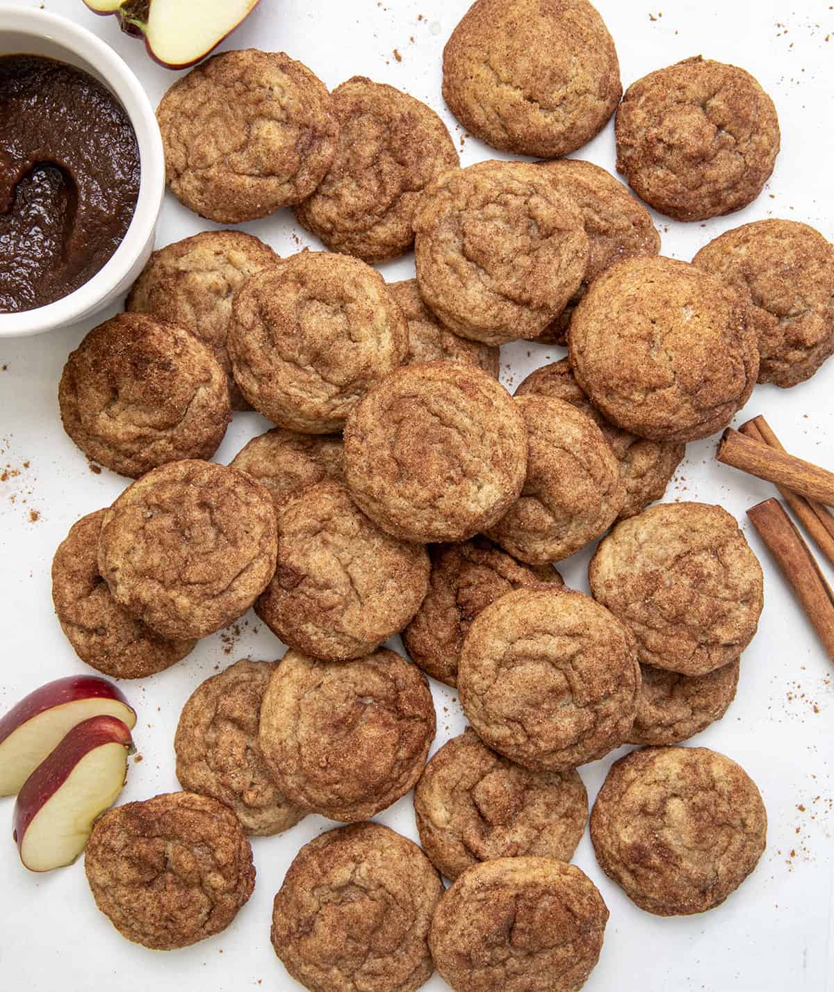 Apple Butter Snickerdoodles on a white table with apple butter, apples, and cinnamon sticks from overhead.