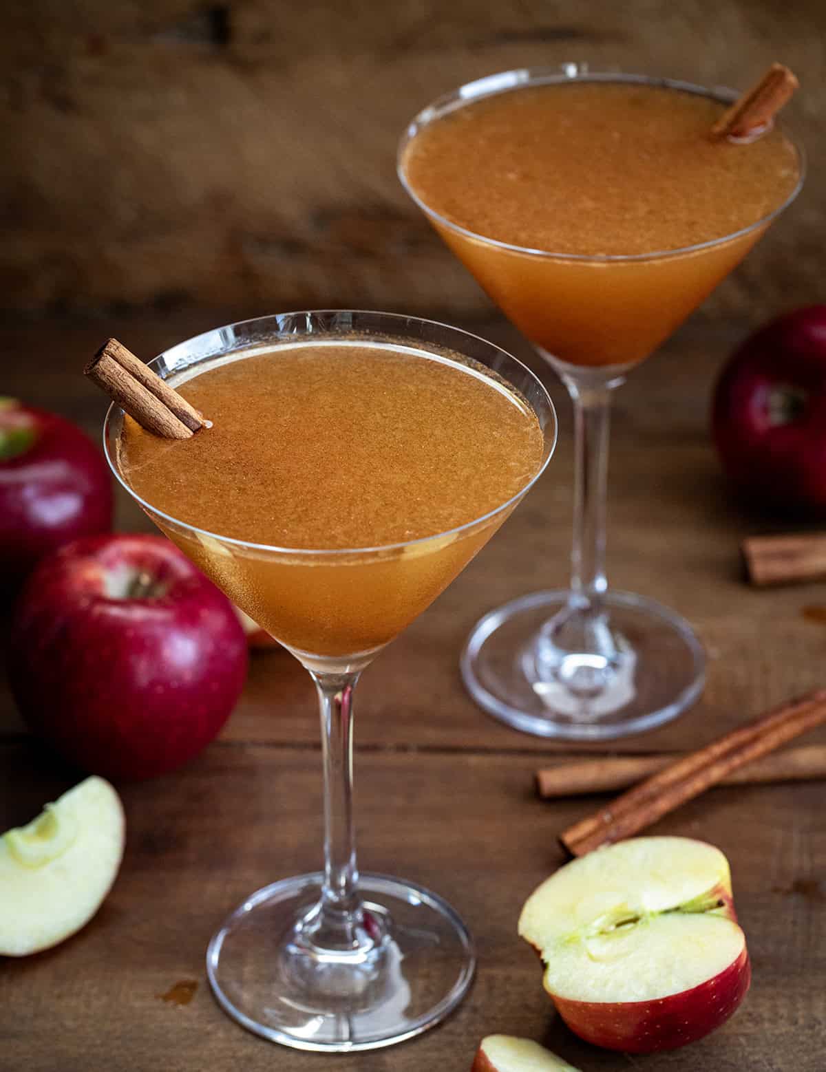 Two Apple Cider Martini's on a wooden table with apples and cinnamon stick.