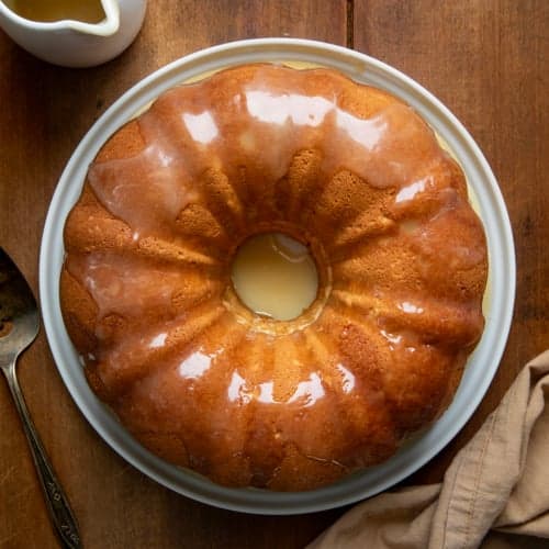 Whole Brown Sugar Maple Pound Cake on a white cake platter on a wooden table from overhead.