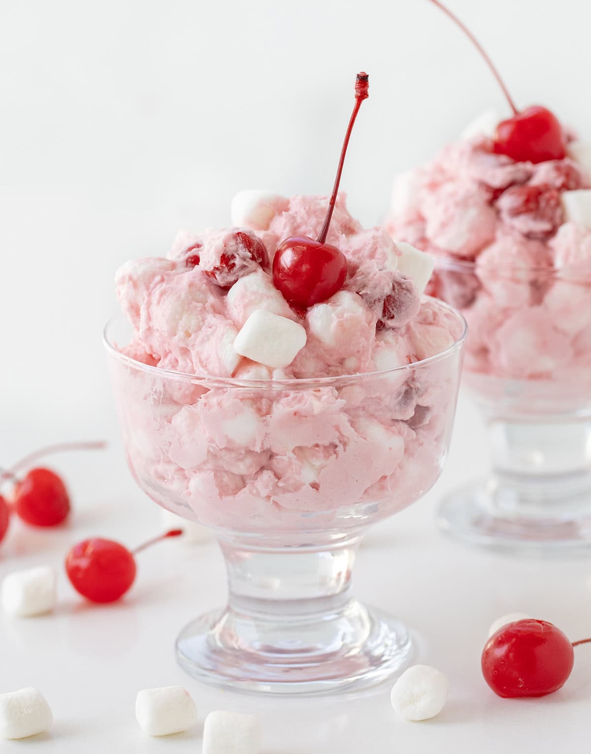 Cherry Cheesecake Fluff in parfait glasses with cherries around on a white table. 