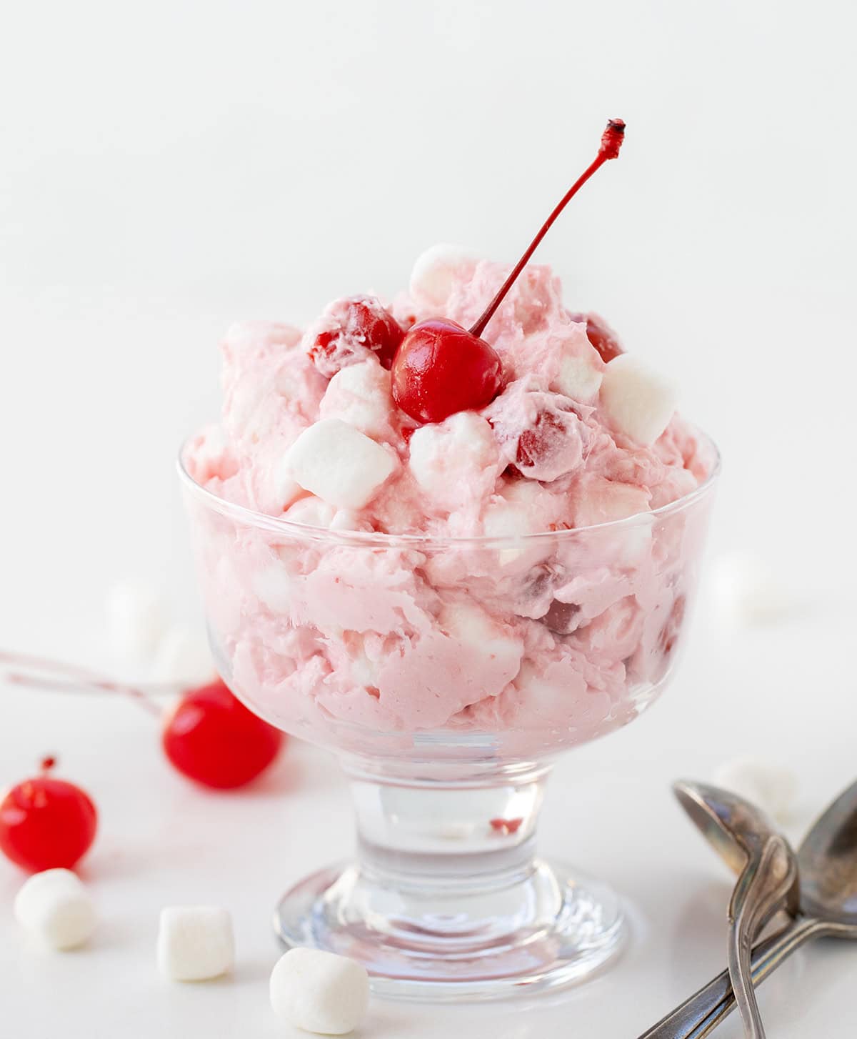 Cherry Cheesecake Fluff in parfait glass with cherries around on a white table.