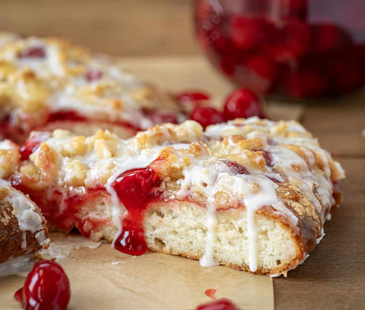 Close up of a slice of Cherry Dessert Pizza on a wooden table with sauce drizzling and cherry pie filling.