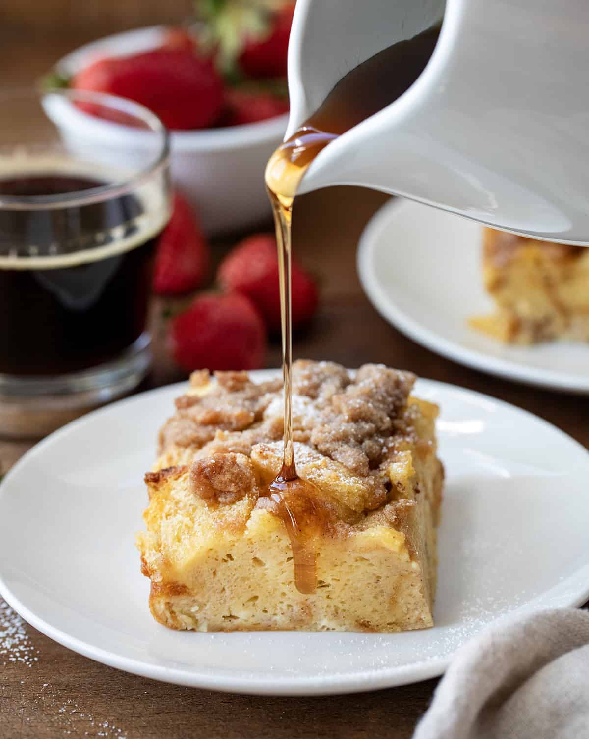 Drizzling syrup over Overnight French Toast Casserole on a white plate.