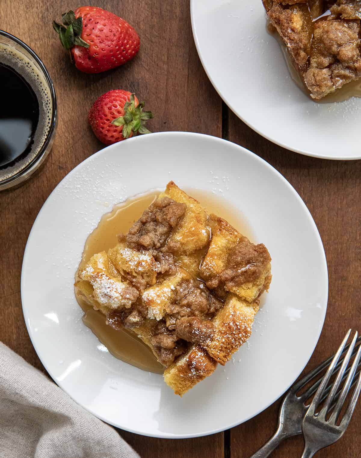 Pieces of Overnight French Toast Casserole on white plates on a wooden table from overhead.