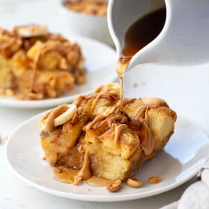 Drizzling syrup over Peanut Butter Banana Overnight French Toast on a white plate.