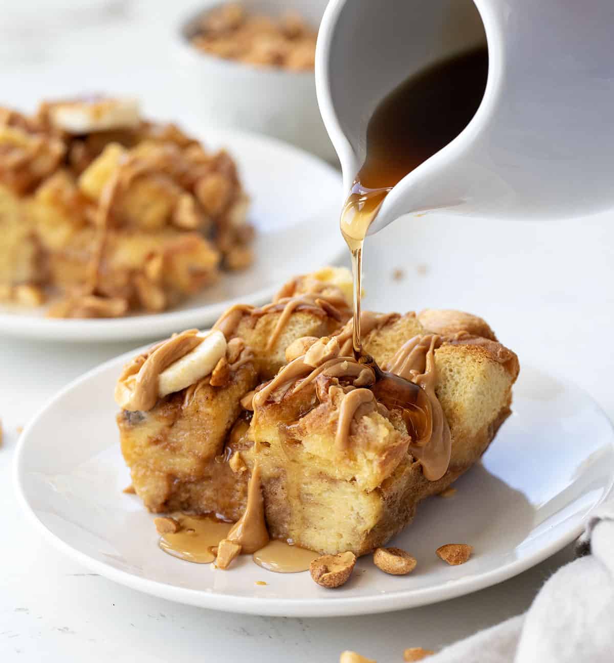 Drizzling syrup over Peanut Butter Banana Overnight French Toast on a white plate.