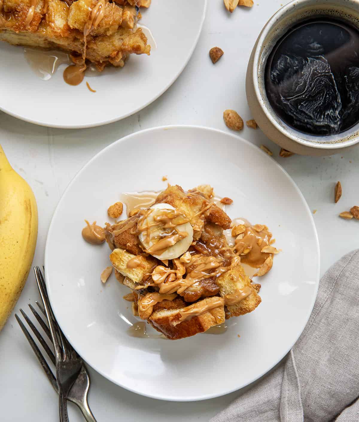 White plates on a white table with Peanut Butter Banana Overnight French Toast on them and forks and coffee from overhead.