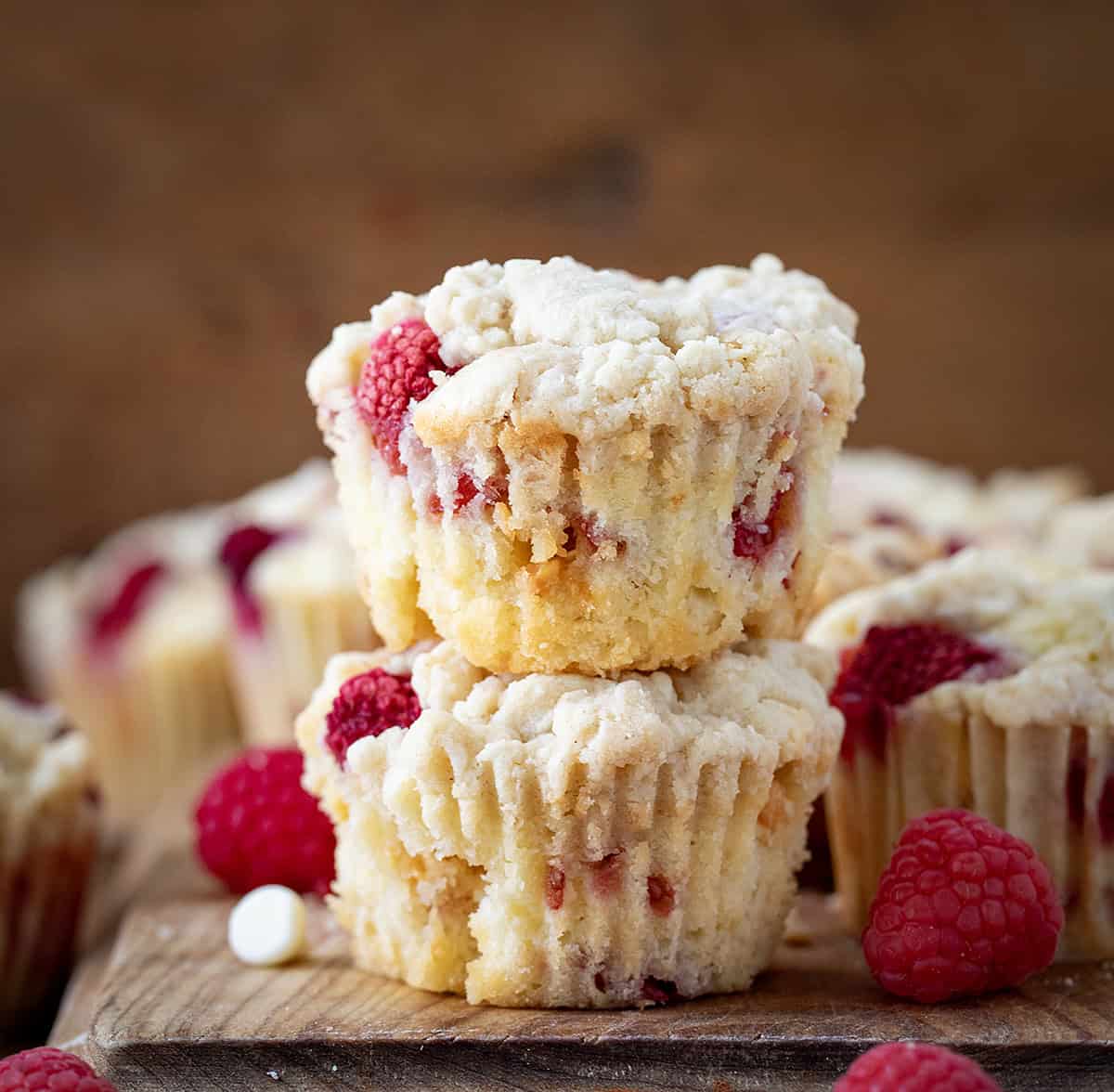 Stacked Raspberry White Chocolate Chip Muffins on a wooden cutting board with raspberries.