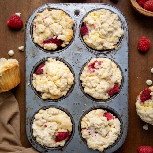 Raspberry White Chocolate Chip Muffins in a muffin tin on a wooden table from overhead.