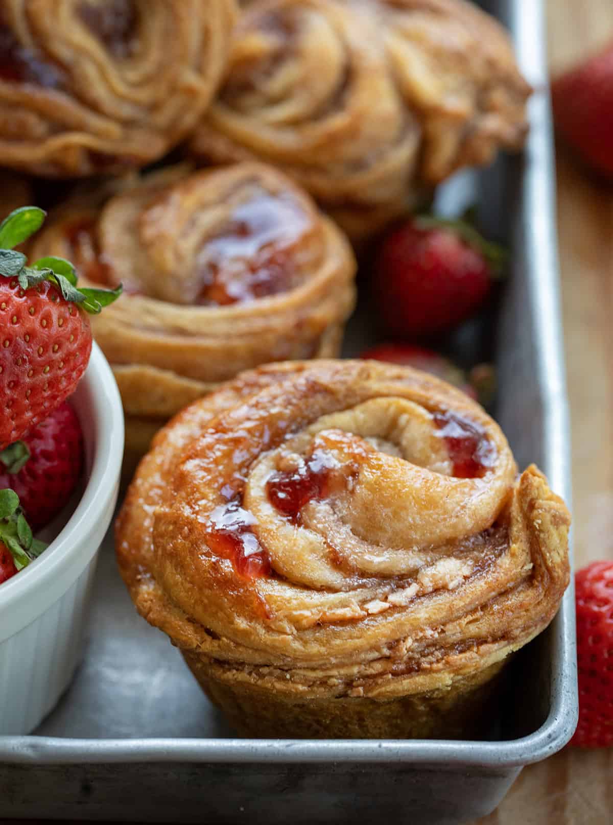 Close up of a Strawberries and Cream Cruffin in a pan with fresh strawberries.