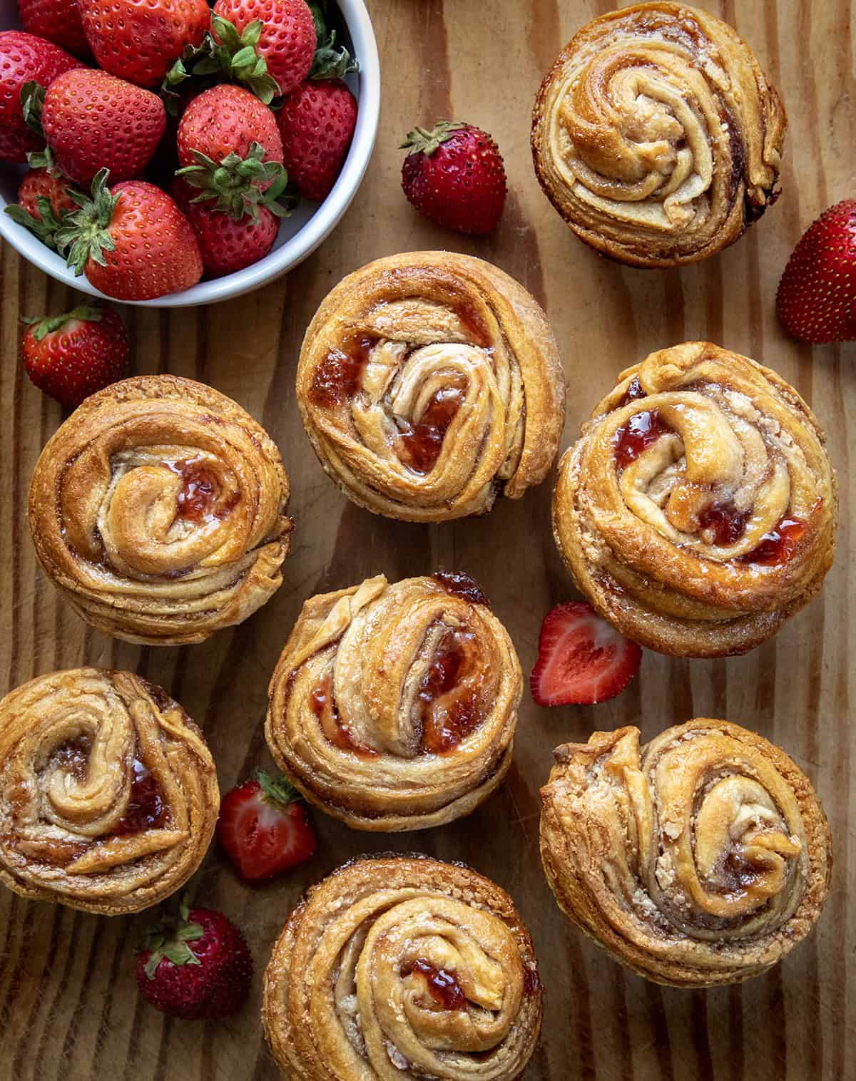 Strawberries and Cream Cruffins laid out on a wooden table with fresh strawberries. 