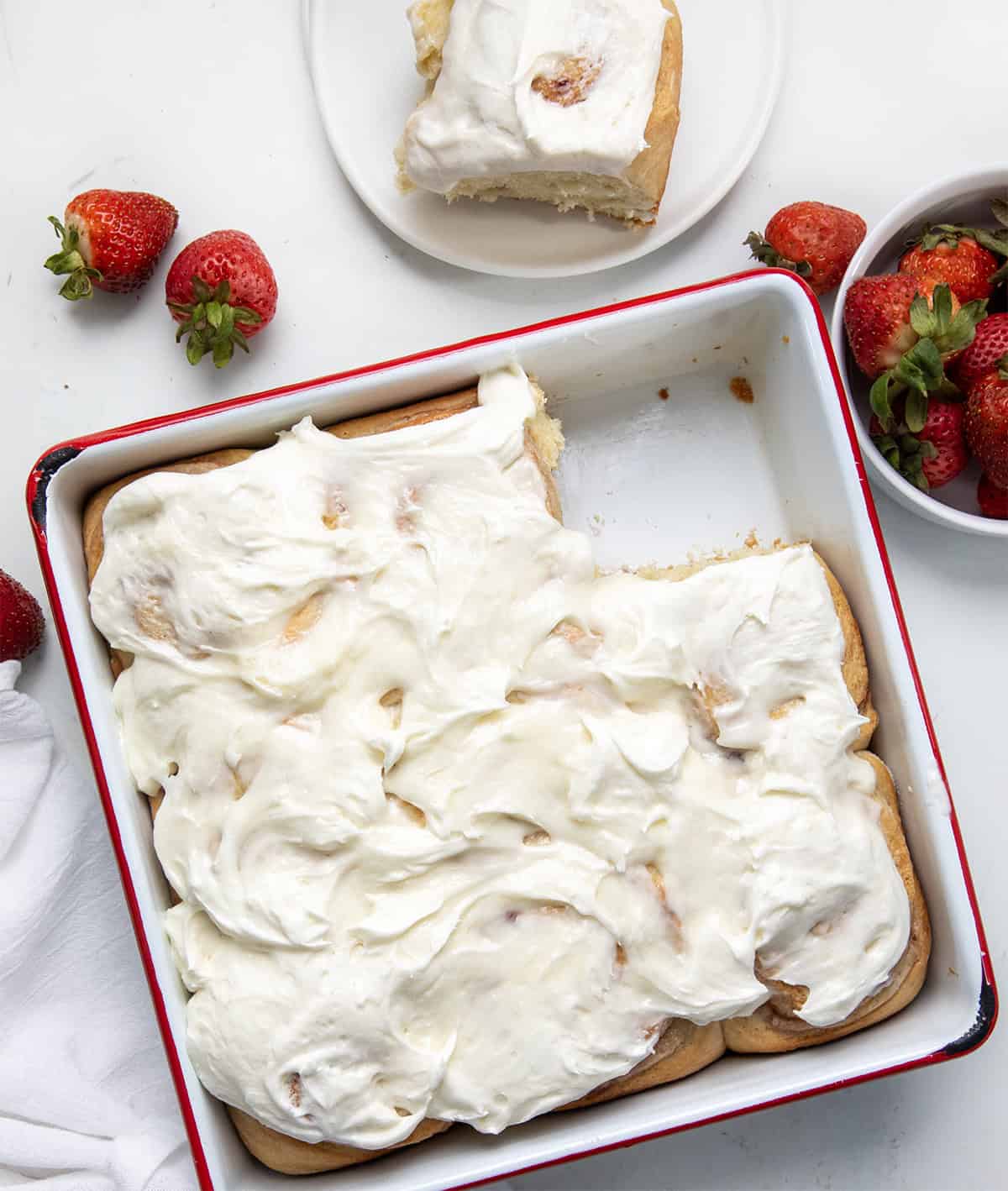 Pan of Strawberries and Cream Sweet Rolls with one missing and on a plate from overhead.