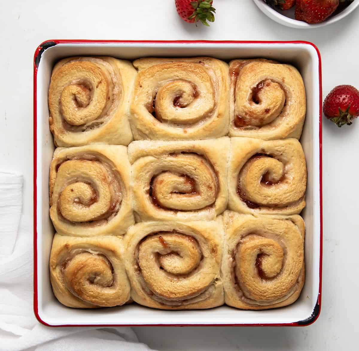 Unfrosted Strawberries and Cream Sweet Rolls on a white table from overhead.