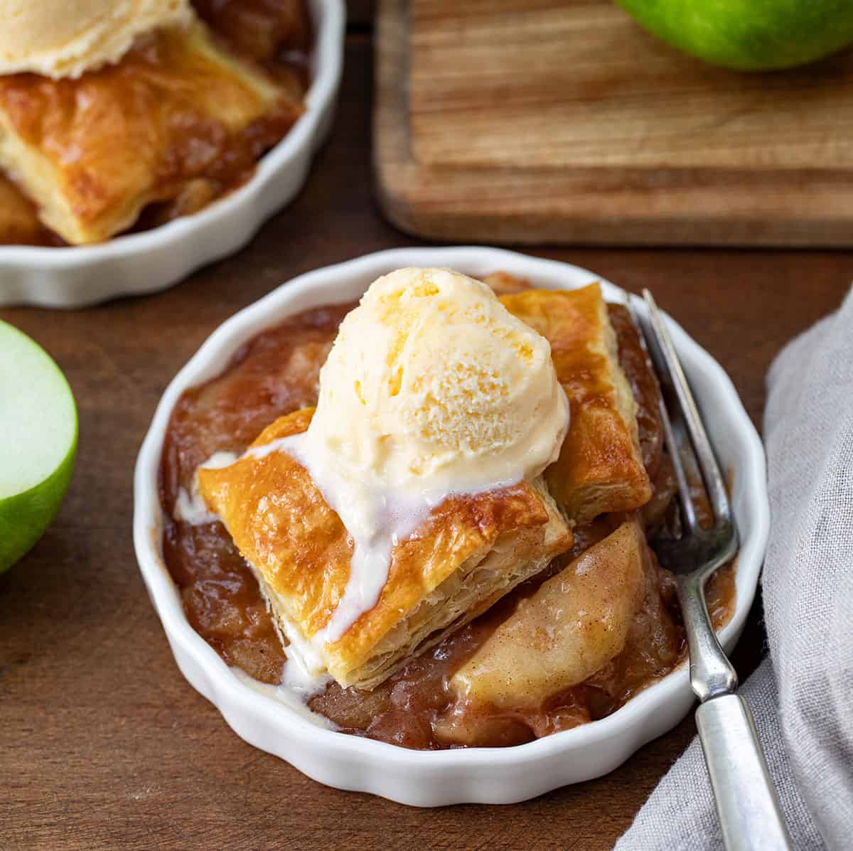 Bowls of Apple Pie Puff Pastry Bake with a fork on a wooden table.