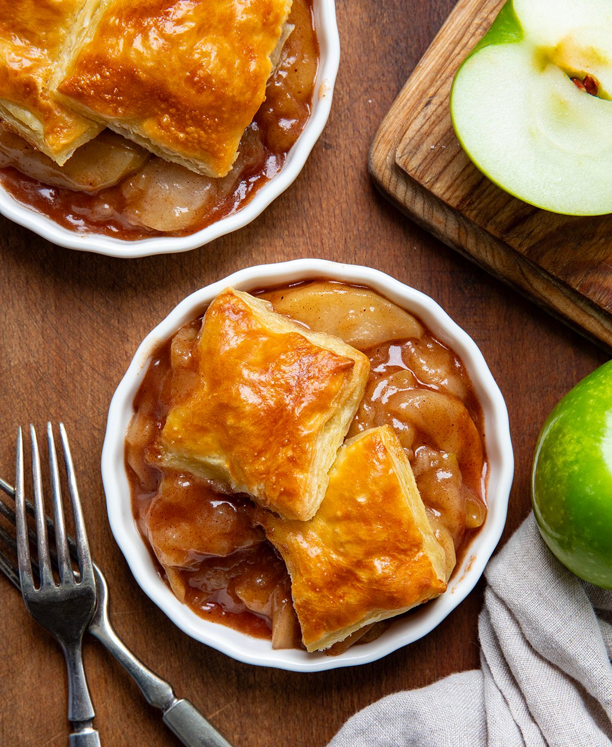 White bowls of Apple Pie Puff Pastry Bake on a wooden table from overhead.