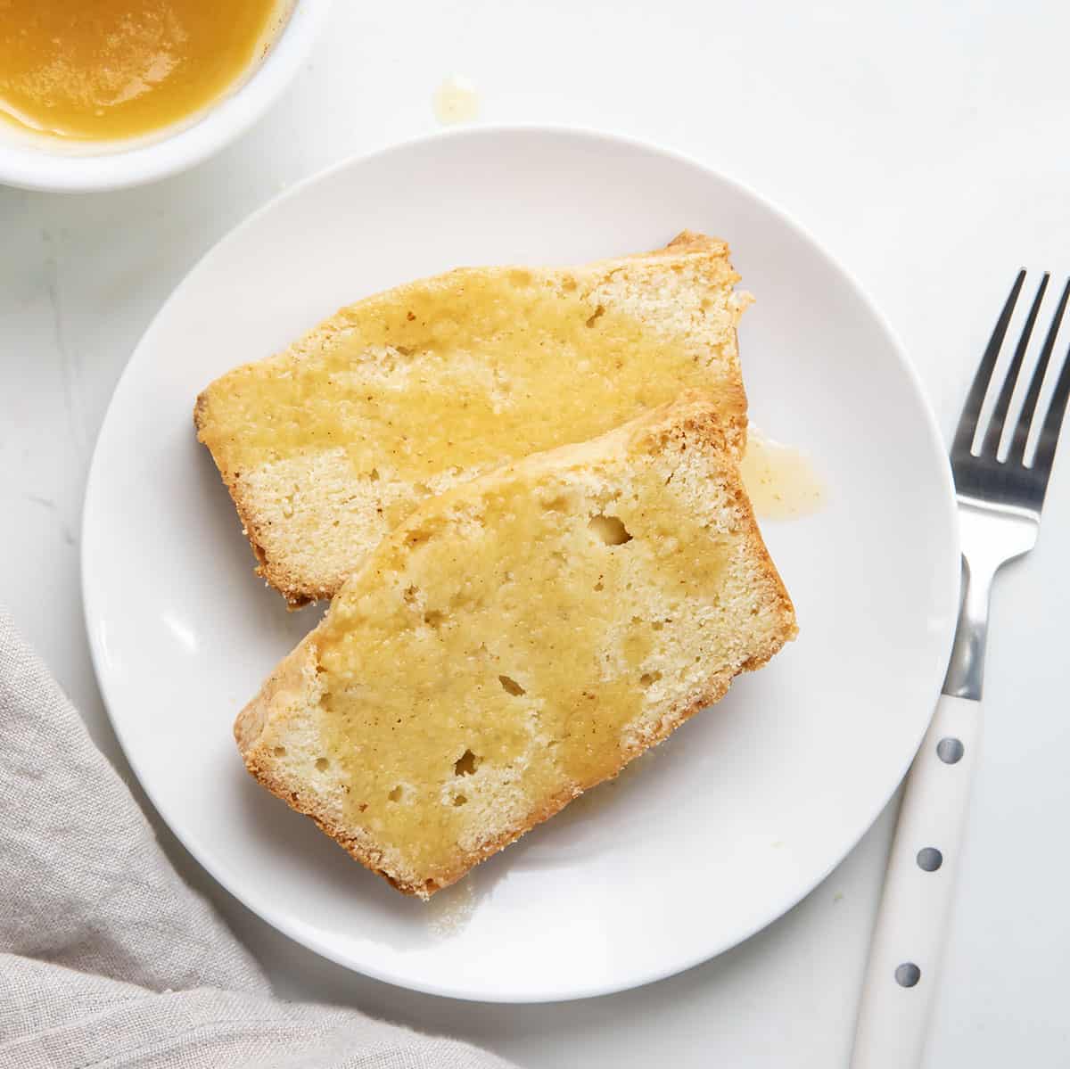 Pieces of Brown Butter Pound Cake on a white plate drizzled with browned butter from overhead.