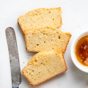 Slices of Brown Butter Pound Cake on a white table with browned butter and a knife.