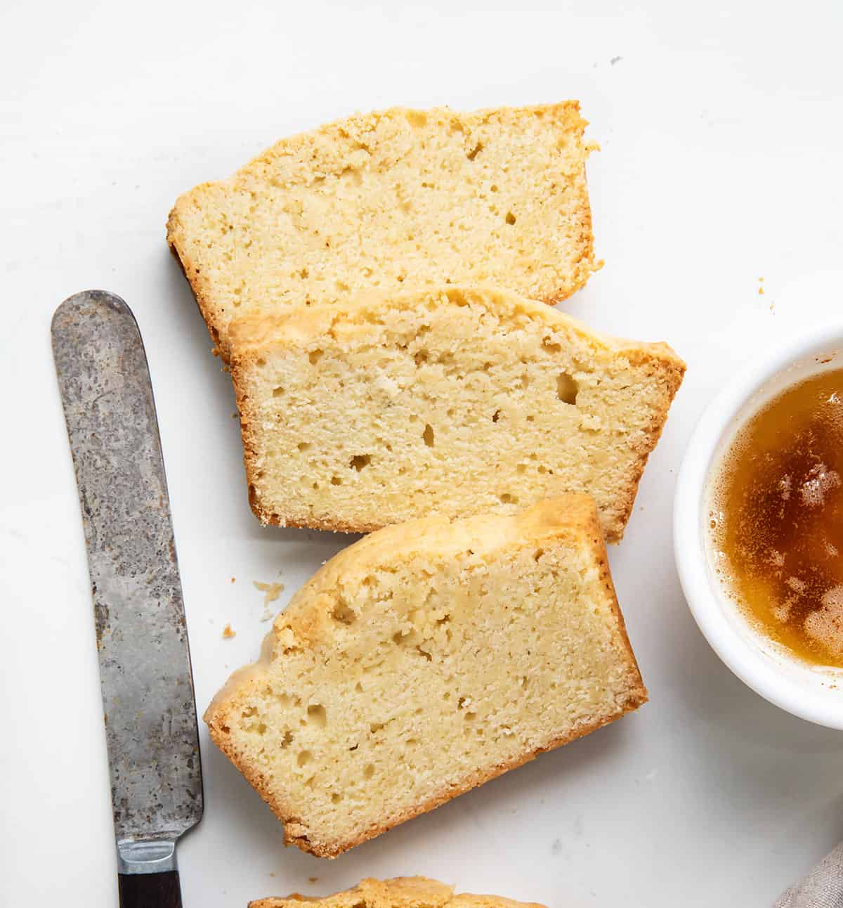 Slices of Brown Butter Pound Cake on a white table with browned butter and a knife.