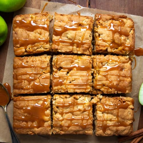 Caramel Apple Snack Cake on a piece of parchment on a wooden table and cut into pieces.